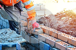 Industrial bricklayer laying bricks on cement mix on construction site. Fighting housing crisis by building more affordable houses