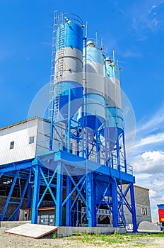Industrial building with big blue tanks for cement, sand, water. Metal stairs leading to metal containers. Vertical photo