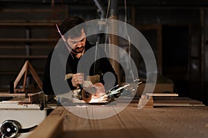 Industrial carpenter worker cutting metal with many sharp sparks at a work bench in a carpentry workshop. Selection focus to