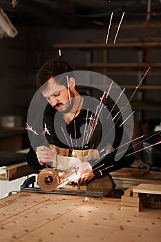 Industrial carpenter worker cutting metal with many sharp sparks at a work bench in a carpentry workshop. Selection focus to