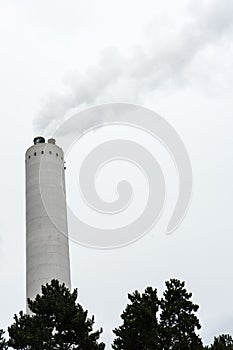 Industrial chimney with smoke with tree in the front
