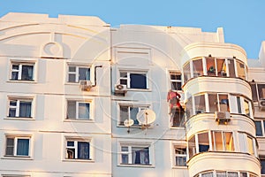 Industrial climber fixed on safety ropes puttying and painting facade of building on sunny day. Bottom view from afar photo