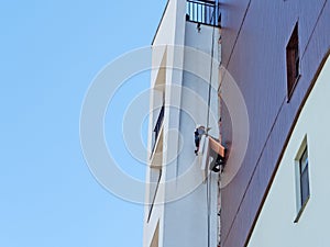 An industrial climber hanging from ropes restores a fragment of a building wall