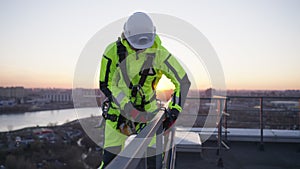 Industrial climber stands on the edge of the roof and ties a rope to descend from the building against the backdrop of