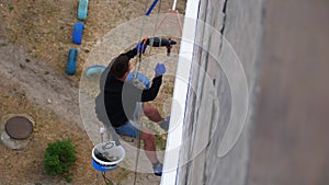 Industrial Climber Suspended on Ropes Insulates Facade with Styrofoam near Wall