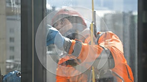 Industrial climber washes windows in an orange jumpsuit in safety gear in slow motion. Washing Windows from dust and