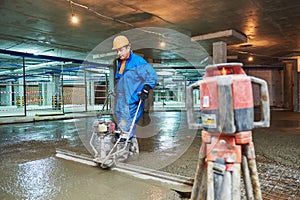 Concrete floor construction. Worker with screeder photo