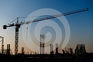 Industrial construction cranes and building silhouettes over sun at sunrise