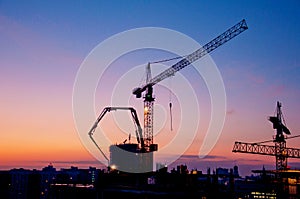 Industrial construction cranes and building silhouettes at sunrise or sunset