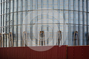 Industrial construction site. Construction of metal cylindrical silos for grain storage. Mechanical cargo winches lift the