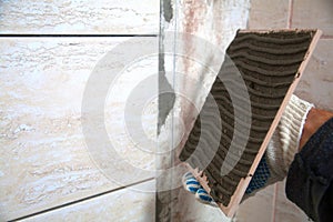 Industrial construction worker installing small ceramic tiles on bathroom walls and applying mortar with trowel