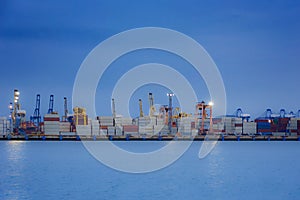 Industrial Container Cargo freight ship with working crane bridge in shipyard at dusk.
