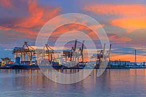 Industrial Container Cargo freight ship with working crane bridge in shipyard at dusk for Logistic Import Export background