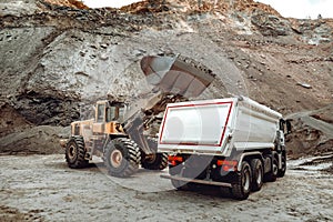 Industrial dumper trucks and wheel loader bulldozer working on highway construction site, loading and unloading gravel and earth.