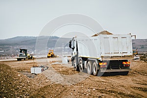 Industrial dumper trucks working on highway construction site, loading and unloading earth. heavy duty machinery activity