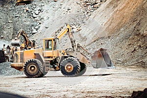 Industrial duty wheel loader on quarry site transporting and loading gravel into dumper trucks