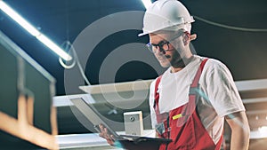 Industrial employee in safety wear is working with a laptop