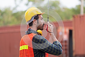 Industrial engineer in hard hat containers box background, Dock worker man talks on two-way radio at containers cargo, Logistic