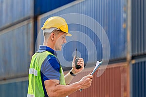 Industrial engineer in hard hat containers box background, Dock worker man talks on two-way radio with holding clipboard checklist