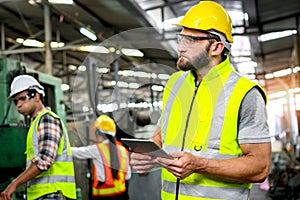 Industrial engineer with helmet and safety vest holds tablet for checking process and machinery machine engine at manufacturing