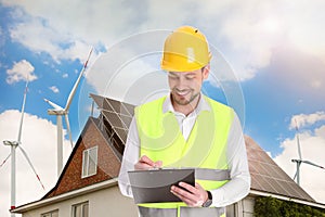 Industrial engineer in uniform and view of wind energy turbines near house with installed solar panels on roof