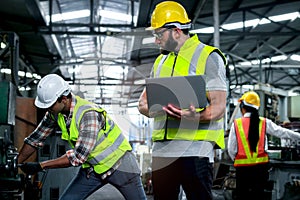 Industrial engineer wearing helmet and safe glasses, holding laptop computer for operating machinery at manufacturing plant