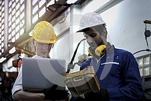 Industrial engineer worker woman and man wearing helmet discussing and working together at manufacturing plant factory, young