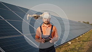 Industrial expert wearing helmet and controlling drone in photovoltaic solar power plant. Solar panel array installation