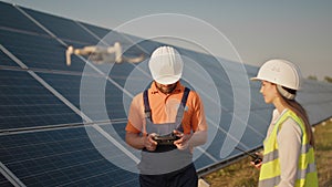 Industrial expert wearing helmet and controlling drone in photovoltaic solar power plant. Solar panel array installation