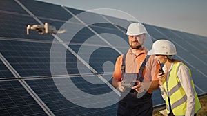 Industrial expert wearing helmet and controlling drone in photovoltaic solar power plant. Solar panel array installation