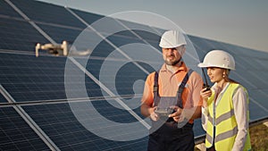 Industrial expert wearing helmet and controlling drone in photovoltaic solar power plant. Solar panel array installation