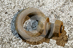 An industrial eyebolt lies on a concrete surface.