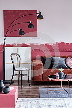 Industrial fashionable lamp next to Chair with magazines next to brown corner sofa with pillows in white and burgundy interior