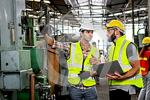 Industrial foreman and worker with helmet and safety vest using laptop computer during discussing together at manufacturing