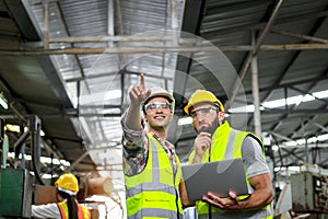 Industrial foreman and worker with helmet and safety vest using laptop computer during discussing together at manufacturing