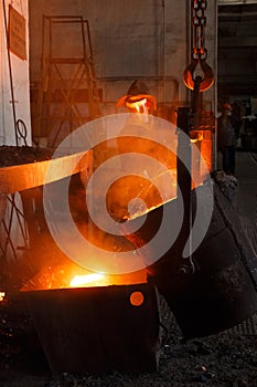 Worker in protective gear pours molten metal at steel mill. Industrial foundry scene showcasing manufacturing process photo