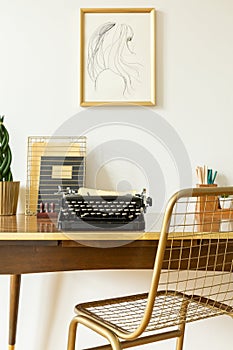 Industrial, golden net chair by a wooden desk with a black, vintage typewriter in an artistic home office interior