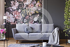 Industrial golden pendant light and black furniture in a dark living room interior with floral wallpaper and a gray couch