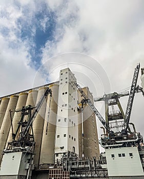 Industrial Grain Silos and Loading Cranes Under Cloudy Sky