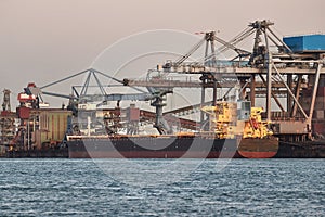 Industrial harbor with rusty structures, bulk carrier ship