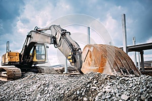 Industrial heavy duty excavator moving gravel on highway construction site. Multiple industrial machinery on construction site