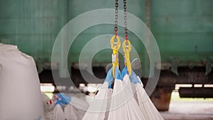 Industrial hooks lifting heavy white bags in a warehouse.