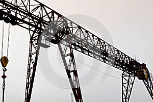 Industrial iron large metal gantry crane with a hook mounted on the supports for lifting and carrying heavy cargo