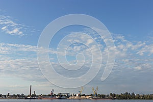 Industrial landscape, cranes, ships and factories on the river bank, against the blue sky