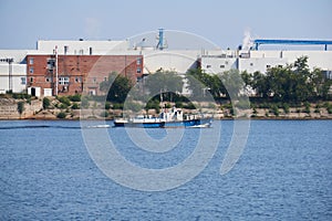 Industrial landscape with a factory on the banks of the river, along which a motorship floats photo