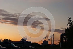 Industrial landscape - orange sunset over a working factory, smoke from the pipes makes purple clouds