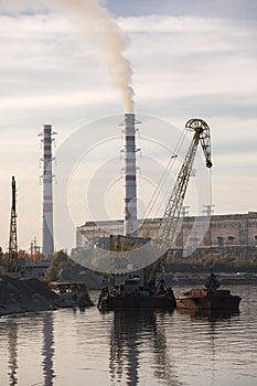 Industrial landscape. River, pipes with smoke and factory. Crane on a barge loads cargo. Smokes from pipes. Industrial area near