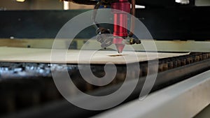 An industrial laser cuts a pattern on a sheet of plywood and moves close-up.