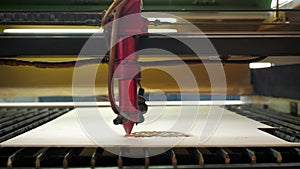 An industrial laser cuts a pattern on a sheet of plywood and moves close-up.