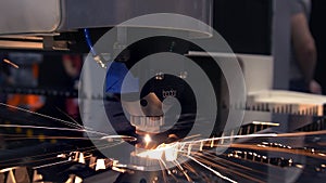 Industrial laser cutter with sparks. The programmed robot head cuts with the aid of a huge sheet of metal temperature. A